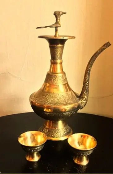 A traditional Nepali brass pot with intricate carvings, accompanied by two brass bowls, used for serving Chhaang, the fermented grain drink.